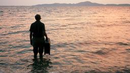 Holger steht mit seinem Koffer am Strand. 