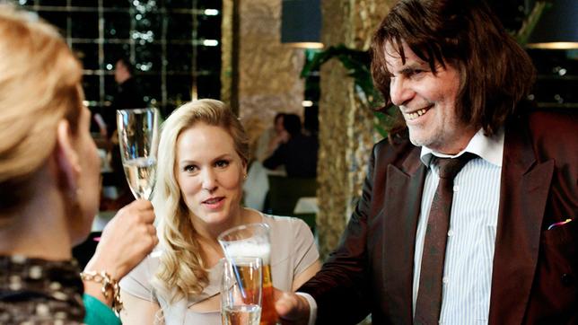 Toni Erdmann (Peter Simonischek) mischt sich in einer Bar ins Gespräch von Ines (Sandra Hüller) und Steph (Lucy Russell, mi.)