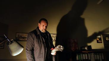 Lemp (Felix Vörtler) holt eine Flasche Schnaps aus der Schublade.