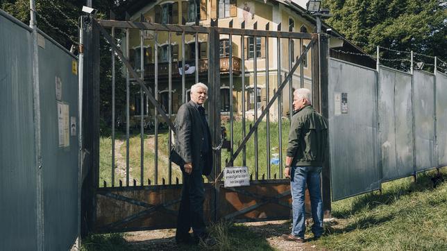 Kriminalhauptkommissar Franz Leitmayr und Kriminalhauptkommissar Ivo Batic stehen vor dem verschlossenen Eingangstor zum "Freiland"-Gelände.