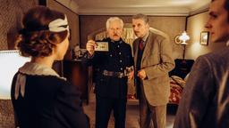 Constable Ivor Partridge (Miroslav Nemec, links) und Chief Inspector Francis Lightmyer (Udo Wachtveitl, rechts) fragen Heather (Marie Rathscheck) und Reverend Teal (Joshua Seelenbinder) in Arthurs Zimmer nach den gefundenen Fotos. 