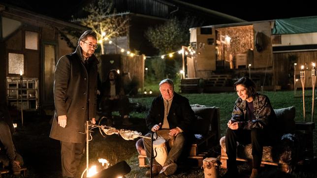 Abend auf dem Erlenhof: Prof. Karl-Friedrich Boerne (Jan Josef Liefers), Kommissar Frank Thiel (Axel Prahl) sitzen mit Inès Fournier (Maëlle Giovanetti) am Lagerfeuer.