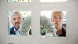 Freddy Schenk und Max Ballauf blicken durch das Fenster einer Hauseingangstür.