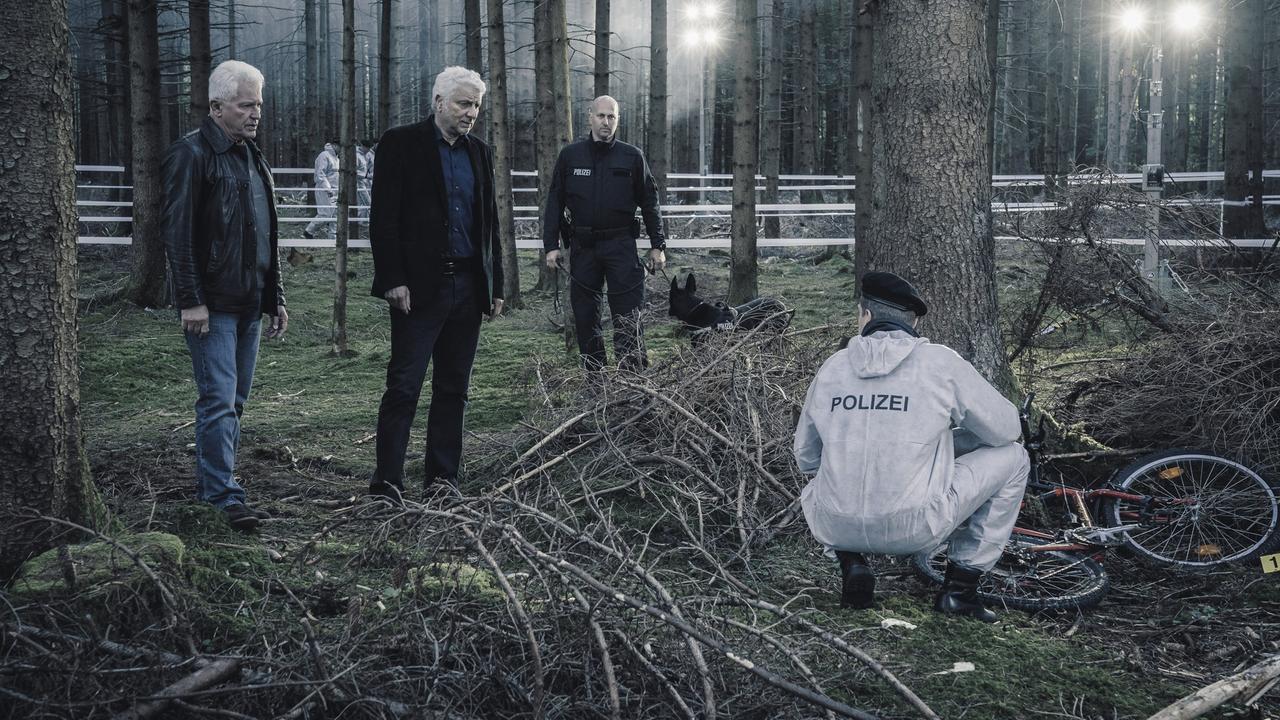 Von links: Die Kriminalhauptkommissare Ivo Batic (Miroslav Nemec) und Franz Leitmayr (Udo Wachtveitl) mit Kollegen (Komparsen) betrachten den Fundort von Emils Fahrrad im Wald in der Nähe eines Parkplatzes.