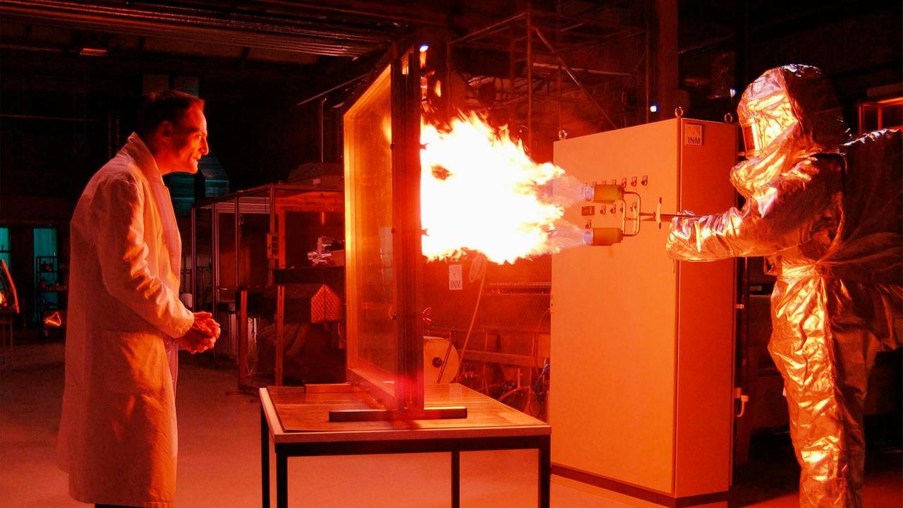 Dr. Fabian Kurz (Dieter Laser) im Testlabor vor einer feuerfesten Glasscheibe.