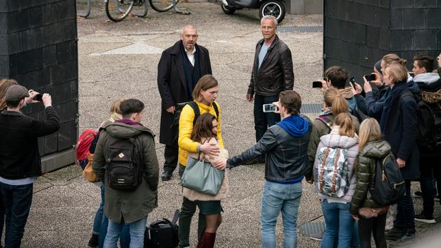 Bild: WDR/Thomas Kost Freddy Schenk (Dietmar Bär, hinten Mitte) muss sich rechtfertigen. Max Ballauf (Klaus J. Behrendt, hinten rechts) sieht zu, wie sein Kollege beschuldigt wird, Nadine Wilcke (Emma Drogunova, vorne) auf dem Schulhof belästigt zu haben. Ihr Freund Lennart (Moritz Jahn) nimmt sie in Schutz, während andere Schüler*innen mit den Handys filmen.