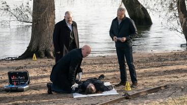 Max Ballauf (Klaus J. Behrendt, r) und Freddy Schenk (Dietmar Bär, l) sind am frühen Morgen am Rheinufer im Einsatz. Rechtsmediziner Dr. Roth (Joe Bausch, kniend) untersucht die Leiche eines Mannes, die hier gefunden wurde.