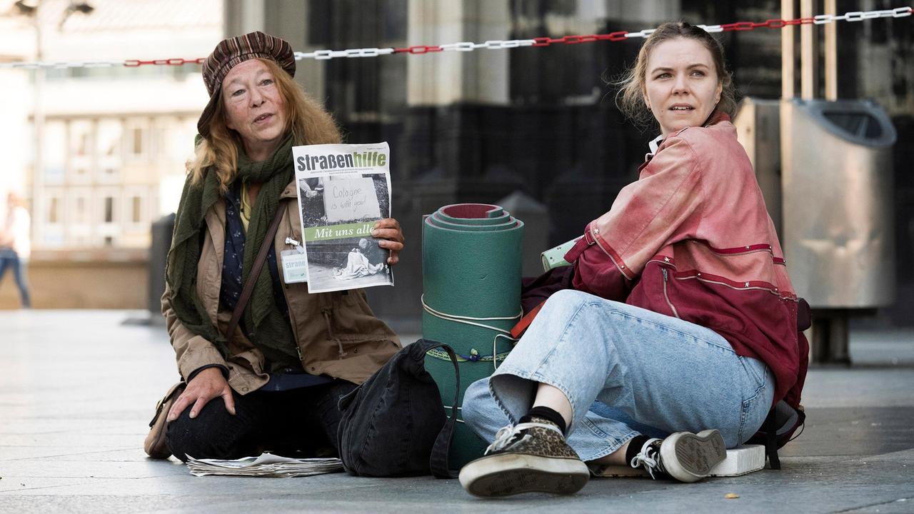 Monika Keller (Rike Eckermann, links) verkauft am Dom Obdachlosenzeitungen. Sie hilft Ella Jung (Ricarda Seifried, rechts), die gerade erst lernt, sich auf der Straße durchzuschlagen.
