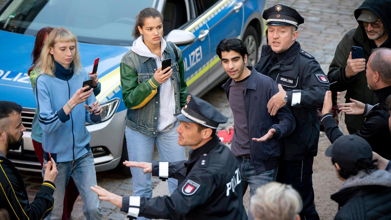 Gibran Hadad (Doguhan Kabadayi) bei seiner Festnahme durch die beiden Polizisten Gerd Wohlers (Josef Heynert, h.) und Ron Hartmann (Peter Sikorski, v.M. mit Kompars:innen).