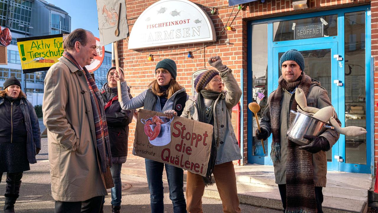 Tierschützer blockieren das Geschäft von Fischhändler Harmsen: Markus Gellert (Herbert Knaup) trifft auf Gundula Mosbacher (Catherine Bode), Gesine Brunken (Anna Böttcher) und Thomas Zuhse (Oliver Wnuk), der sich den Demonstrantinnen angeschlossen hat.