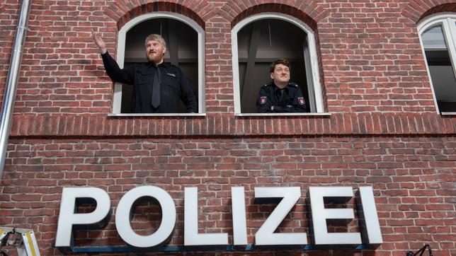 Bild: ARD/Thorsten Jander Außenfassade mit Schriftzug "Polizei", Marc Zwinz (l.) und Sven Fricke (r.) schauen nach der Studiobesichtigung aus dem Fenster ihrer neuen Wache.