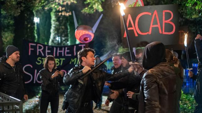 Die Situation eskaliert: Es kommt zu einem tätlichen Übergriff zwischen Daniel Schirmer (Sven Fricke) und einigen Demonstranten (Kompars:innen).