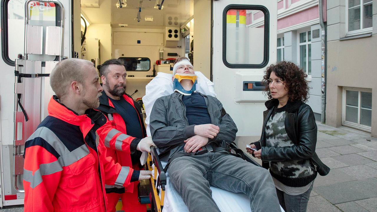 Harry Möller (Maria Ketikidou) konnte dem Unfallopfer Florian Rösner (Lukas Zumbrock, liegend) erste Fragen stellen, dann bestehen die Sanitäter (Komparsen) darauf, ihn abzutransportieren.