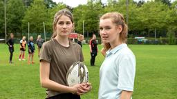 Vanessa Schübel (Marleen Quentin) und Lea Jansen (Louisa Kruse) bemerken, dass ihnen auch ungebetene Gäste beim Rugby zusehen (mit Kompars:innen, h.).