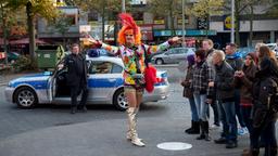 Olivia Jones (M.) startet mit einer Gruppe von Touristen ihre berühmte Kiez-Tour. Dafür hat sie ihre High Heels gegen spaziertaugliche goldene Stiefel eingetauscht. Dirk Matthies (Jan Fedder, l.) und Paul Dänning (Jens Münchow, im HG) kommen im Streifenwagen 14/2 angefahren um Olivia klarzumachen: "Der Kiez ist unser Revier"!.