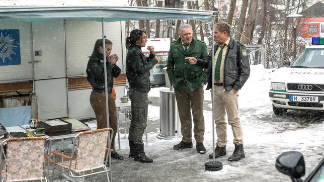 Bild: ARD/TMG/Chris Hirschhäuser Das Team berät über den aktuellen Fall vor dem provisorischen Wohnwagen-Revier, während der Verdächtige mit seinem Anwalt spricht. V.l.n.r. Rebecca (Jeanne Goursaud), Sabine Kaiser (Katharina Müller-Elmau), Girwidz (Michael Brandner), Hubert (Christian Tramitz).