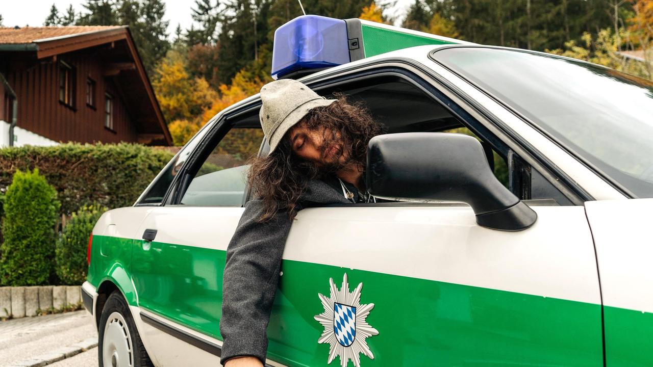 Der Oktoberfest-Tourist Spyros Karamanlis (Nikos Laskaris) ist stark betrunken und wird im Polizeiauto zu seiner Unterkunft gebracht.
