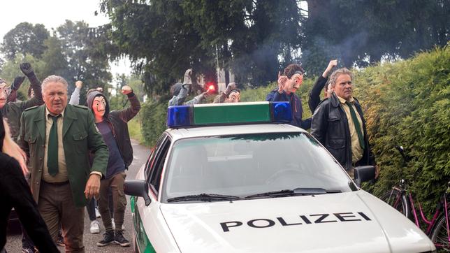 Bild: ARD/Chris Hirschhäuser Hubert (Christian Tramitz) und Girwidz (Michael Brandner) werden zu einem Einsatz gerufen- eine wütende Gruppe von Demonstranten (Komparsen) hat sich vor einem Haus versammelt.