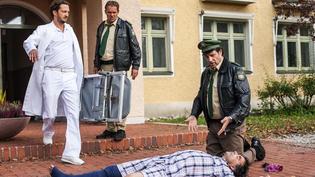Bild: ARD/TMG/Arvid Uhlig Hubert (Christian Tramitz) und Staller (Helmfried von Lüttichau) statten ihrem Kollegen Riedl einen Krankenbesuch ab. Doch aus der netten Aufmunterung wird nichts: ein Patient stürzt sich aus einem der oberen Stockwerke. Dr. Dieter Klemm (Jan Messutat) kommt mit einer Trage, um den Schwerverletzten (Komparse) zu bergen.