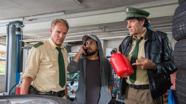 Bild: ARD/TMG/Marco Meenen Mike Schulz (Zejhun Demirov) versucht den Besitzer der Tankstelle telefonisch zu erreichen. Hubert (Christian Tramitz) und Staller (Helmfried von Lüttichau) haben ihn aber schon gefunden – er liegt tot zwischen den Reifen.