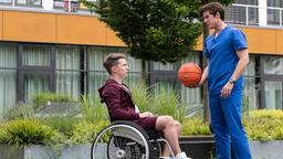 Moritz im Rollsstuhl auf dem Basketballplatz. Ben spricht mit ihm. 