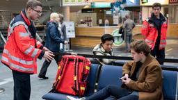 Die Streithähne Nick Jauer (Xidou Zhao) und Marvin Verl (Joscha Eißen) sitzen am Flughafen fest und werden von Ben Ahlbeck (Philipp Danne, h.) und Elias Bähr (Stefan Ruppe) versorgt (mit Kompars:innen).