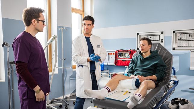 Bild: ARD/Michael Kremer Dr. Ben Ahlbeck (Philipp Danne) und Oliver Probst (Arne Kertész) nehmen den Patienten Patrick Lesser (Andreas Warmbrunn) in der Notaufnahme auf, den Olli noch aus Schulzeiten kennt.