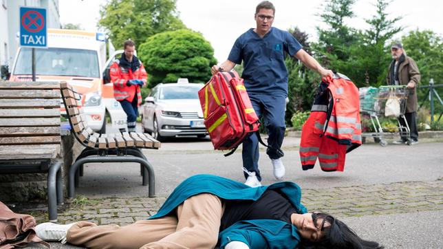 Bild: ARD/Jens-Ulrich Koch Dr. Elias Bähr (Stefan Ruppe, h.M. mit Komparsen) eilt seiner Ex-Frau Ameena Schneider (Mira Mazumdar) zur Hilfe.