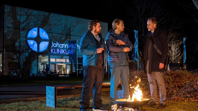 Dr. Kai Hoffmann (Julian Weigend) begutachtet mit David Paulsen (Jan Niklas Berg) ungläubig Dr. Mikko Rantalas (Luan Gummich) vermeintlich erfolgreiche Behandlungsmethode. Ist das etwa doch kein Hokuspokus?