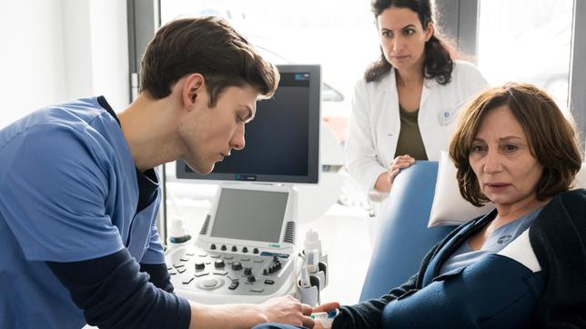 Bild: ARD/Jens Ulrich Koch Es gibt einen Neuzugang am Johannes-Thal-Klinikum: Assistenzarzt Florian Osterwald (Lion Wasczyk) darf, unter der Aufsicht von Leyla Sherbaz (Sanam Afrashteh, h.) seine erste Patientin untersuchen. Alina Petrowa (Marina Weis) ist von der Treppe gestützt, kann sich aber nicht mehr daran erinnern.