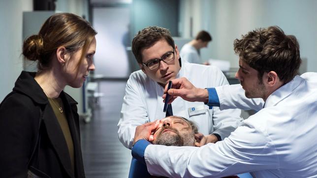 Bild: ARD/Jens Ulrich Koch Gero (Nicki von Tempelhoff) hat kurz nach der Einlieferung ins JTK das Bewusstsein verloren. Elias Bähr (Stefan Ruppe, h.) und Dr. Niklas Ahrend (Roy Peter Link) entscheiden, er muss sofort in den OP. Geros Frau Christine (Nike Fuhrmann) bangt um das Leben ihres Mannes.