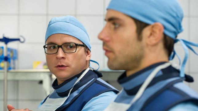 In aller Freundschaft – Die jungen Ärzte:  Elias Bähr (Stefan Ruppe) und Dr. Ahrend (Roy Peter Link) machen sich für Daniel Ruhlands Bein-OP steril.