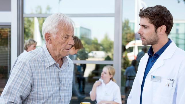 Niklas (Roy Peter Link) ist überrascht: Vor ihm steht plötzlich Otto Stein (Rolf Becker, l. mit Komparsen im HG), ein alter Bekannter aus der Sachsenklinik in Leipzig. Er schöpft sogleich Verdacht: leidet Otto an Parkinson?