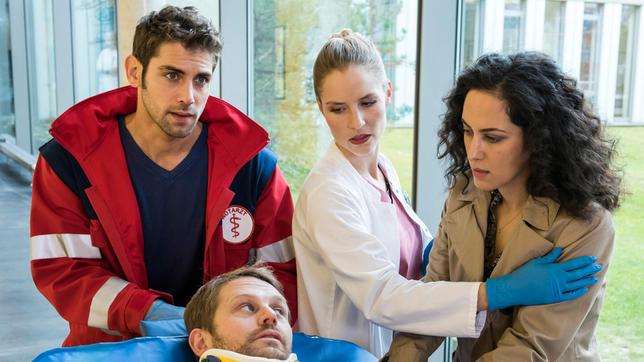 Bild: ARD/Jens Ulrich Koch Raik Hoffmann (Tim Ehlert) wurde nach einem Sturz vom Hochspannungsmast ins JTK gebracht; seine Frau Linda (Damineh Hojat) will ihm beistehen. Dr. Niklas Ahrend (Roy Peter Link) und Julia Berger (Mirka Pigulla) müssen den Verletzten sofort zur Untersuchung bringen.