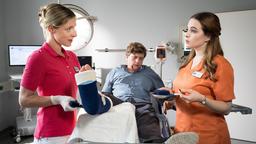 Während Alexandra (Friederike Linke) den Unterschenkel des Patienten Peter Flemming (Philippe Graber) eingipst, prüft sie Jasmins (Leslie-Vanessa Lill) Wissen.