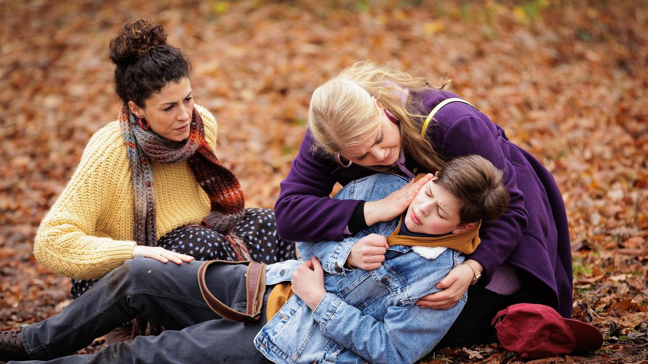 Miriam Schneider (Christina Petersen, re.) und ihre Frau Rieke Machold (Liza Tzschirner, li.) drehen eine Kennenlern-Runde im Park mit ihrem potenziellen Pflegekind Cosmo (Max Bär, liegend). Doch plötzlich bricht der 13-Jährige mit akuter Atemnot zusammen.