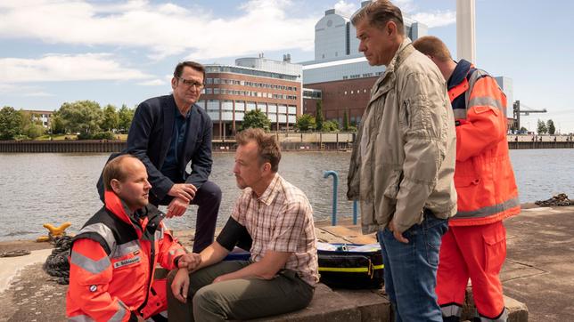 Bild: ARD/Georges Pauly Alexander Hoffmann, ein Ex-Trinker, wurde in seinem Haus am Wasser niedergestochen und tödlich verletzt. Die Lübecker Ermittler Finn Kiesewetter (Sven Martinek) und Lars Englen (Ingo Naujoks) müssen das Verbrechen aufklären. Was hat Bernd Reuter (Christian Bruhn, 3.v.l. mit Komparsen) damit zu tun.