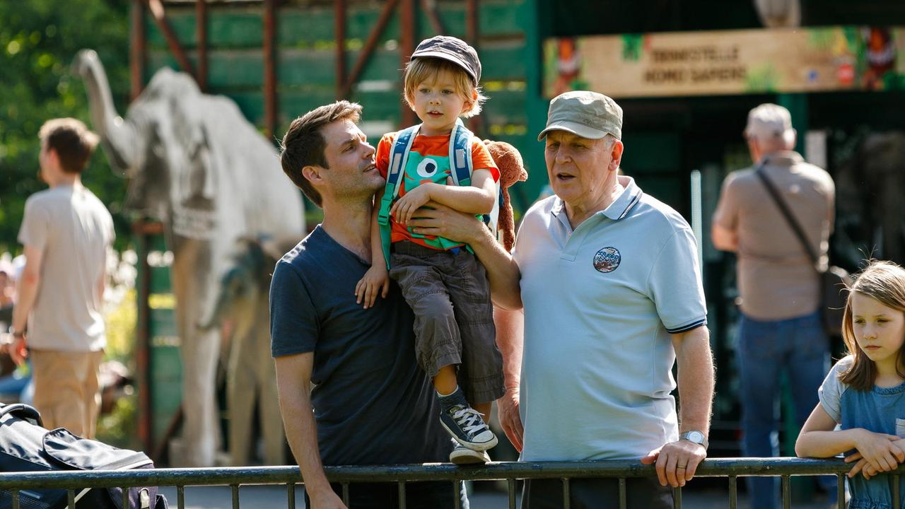 Finn (Florian Thürnagel) besucht mit Papa Thomas (Sebastian Schlemmer) und Opa Georg (Stefan Viering) den Zoo (mit Komparsen).
