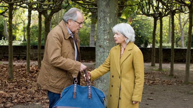 Klaus Schmitz (Hartmut Volle) nimmt Giselheid (Ilona Schulz) die Tasche ab. Wird sich seine Vermutung über deren Inhalt bestätigen?