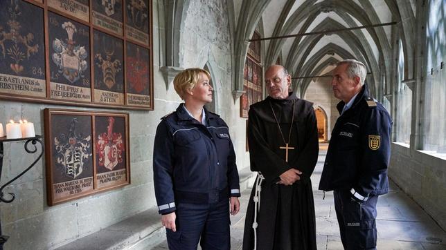 Bild: ARD/Dominik Hatt Paul Schott (Tim Wilde) und Nele Fehrenbach (Floriane Daniel) treffen Abt Barnabas (Ulrich Gebauer) im Kreuzgang von Kloster Oberzell.