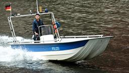 Frank van Dijk (Niklas Osterloh) inspiziert vom Boot aus das Ufer.