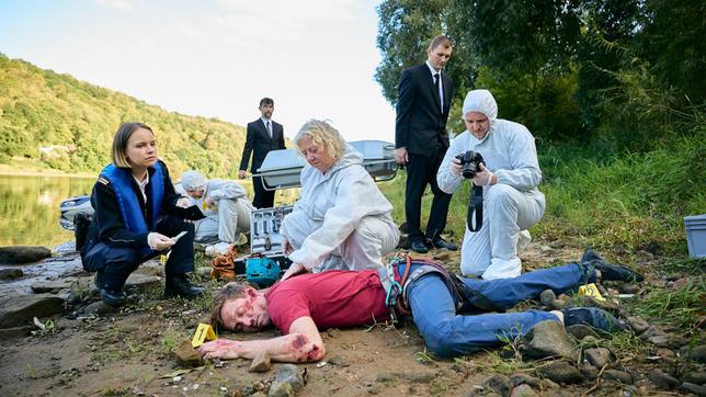 Bild: ARD/Rudolf Wernicke Tonis Leichnam wird gerade von Dr. Jaschki (Regine Hentschel, mi.) und Kommissarin Macourek (Barbara Prakopenka, li.) untersucht. Während KTU’ler (Komparserie) die Fundstelle absuchen und Fotos machen.