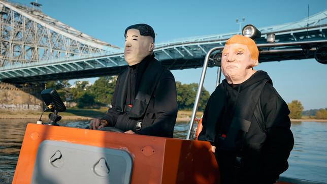 Bild: ARD/Rudolf Wernicke Zwei maskierte Personen, jeweils als Trump und Kim Jong Un fahren mit einem Motorboot.