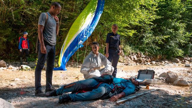 Bild: ARD/Lucky Bird Pictures/Angela Schablitz Der Profi-Paraglider Mike Bischoff ist in den Tod gestürzt. War es kein Unfall? Die Ermittlungen der Kommissare bestätigen zunehmend diese These. V.l.n.r. Jerry Paulsen (Peter Marton), Pathologin Sonja Bitterling (Genoveva Mayer), Caro Reiser (Sarah Thonig) und Komparsen