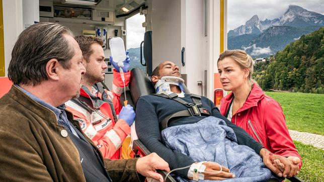 Bild: ARD/Lucky Bird Pictures/Andreas Steffan Jerry Paulsen (Peter Marton, liegend) hatte einen Unfall: An seinem Dienstwagen haben die Bremsen versagt. Johanna (Ines Lutz) und ihr Vater Benedikt Beissl (Andreas Geibel) sind zur Stelle, wie der verletzte Jerry in den Krankenwagen geladen wird. Sanitäter (Komparse)
