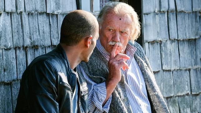 Jerry Paulsen (Peter Marton) sitzt mit Josef Lahner (Franz Buchrieser) vor dessen Hütte auf der Bank - der vertraut ihm ein dunkles Geheimnis an.