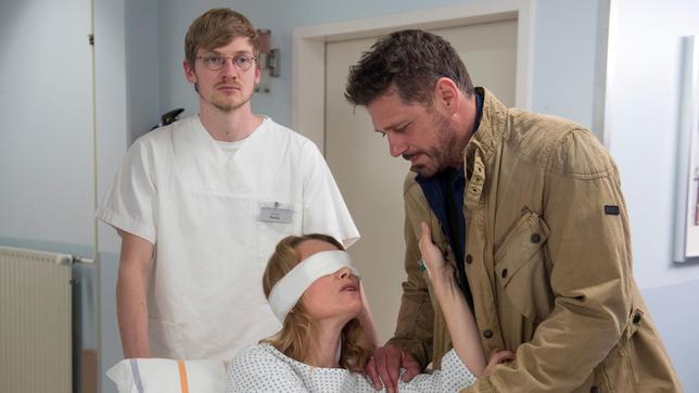 Nach der Augen-OP versucht Eva (Andrea Lüdke, l. mit Björn Bugri, r. und Komparse, h.) sich zu erinnern, was es mit der Nachricht auf ihrem Handy auf sich hat.