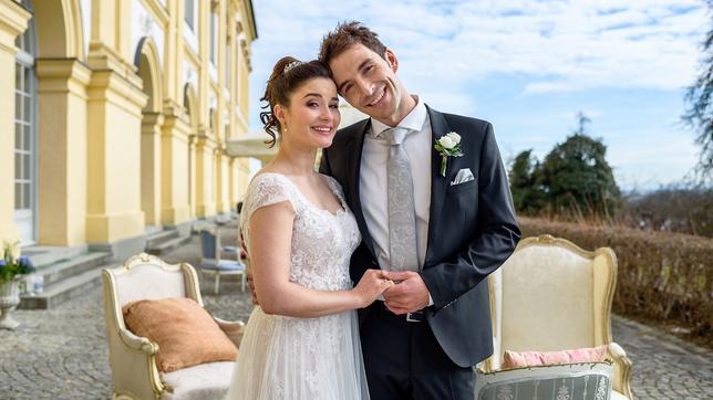 Clara Morgenstern (Jeannine Wacker) und Adrian Lechner (Max Alberti) im Brautkleid und Anzug vor dem Schloss