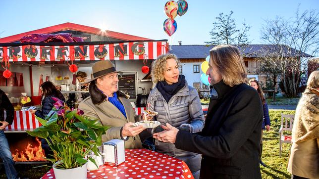 Bild: ARD/Christof Arnold Die Eröffnung des Currywurststandes im Dorf nutzt André (Joachim Lätsch) geschickt aus, um Werbung für sich zu machen. Während Michael (Erich Altenkopf) sich hinreißen lässt, die Currywurst zu probieren, hat Natascha (Melanie Wiegmann) genug gesehen (mit Komparsen im Hintergrund).
