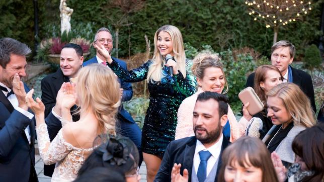 Bild: ARD/Christof Arnold Hochzeit: Christoph (Dieter Bach), Alicia (Larissa Marolt) und die Hochzeitsgäste genießen den Auftritt von Schlagerstar Beatrice Egli (h.) in vollen Zügen.